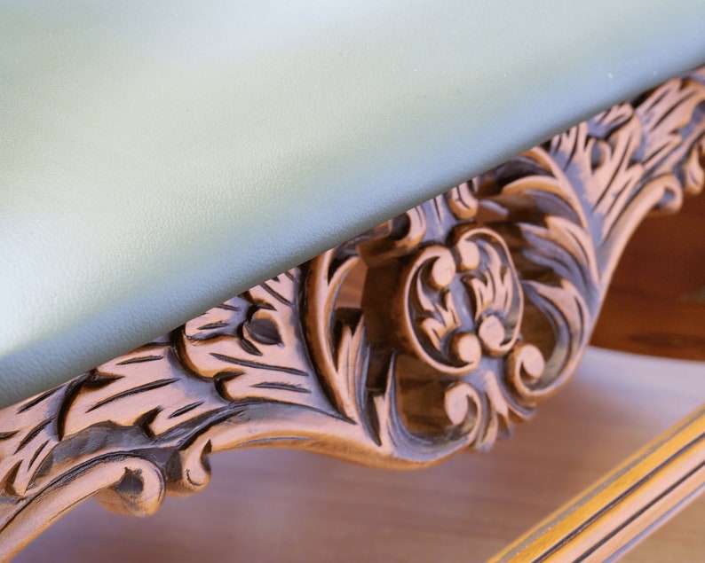 May include: A wooden table with a light green top and intricate carved details around the edge. The carving features a floral design with a central motif of three rounded shapes.