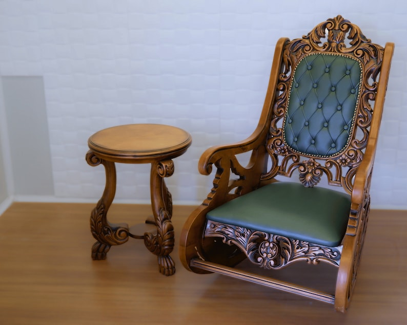 May include: A wooden rocking chair with intricate carvings and a green upholstered seat. A small wooden table with a round top sits next to the chair.
