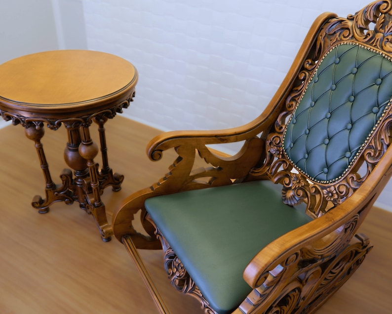May include: A wooden rocking chair with intricate carvings and a green upholstered seat. A matching wooden table with a round top sits next to the chair.