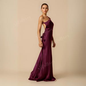 Pode incluir: Um vestido longo de cetim bord&ocirc; de um ombro s&oacute;, com costas abertas e um detalhe de n&oacute; na cintura.
