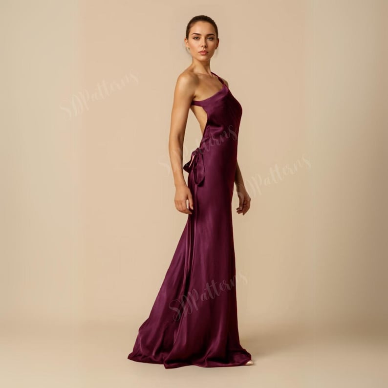 Pode incluir: Um vestido longo de cetim bord&ocirc; de um ombro s&oacute;, com costas abertas e um detalhe de n&oacute; na cintura.
