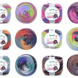 Könnte beinhalten: Zwölf Knäuel Lucky Soft Garn der Marke "gründl", jedes mit einer einzigartigen Farbmischung. Das Garn ist eng gewickelt, mit Farbtönen von Rosa, Lila, Grün, Blau, Orange und Braun. Die Etiketten auf den Garnknäueln sind deutlich sichtbar.