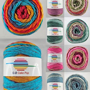 Könnte beinhalten: Eine Auswahl an bunten Garnkuchen in verschiedenen Farbtönen, darunter Blau, Orange, Rot und Grün. Jeder Garnkuchen ist mit "G-B Cake Pop" beschriftet und hat ein Regenbogen-Design. Ideal für Strick- und Häkelprojekte.
