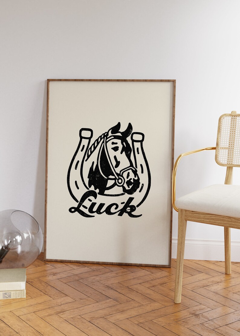 May include: Black and white illustration of a horse's head inside a horseshoe with the word "Luck" printed below. The illustration is on a beige background and framed with a light brown wood frame.
