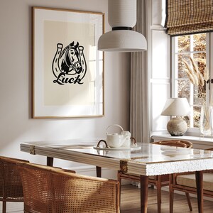 May include: A black and white illustration of a horse's head inside a horseshoe with the word "Luck" printed below. The illustration is framed and hanging on a wall in a dining room with a white table and wicker chairs.
