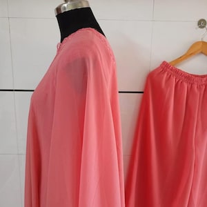 May include: A coral-colored, two-piece outfit displayed on a mannequin and a hanger. The top has a round neckline with lace trim. The pants have an elastic waistband. The fabric appears lightweight and flowing.