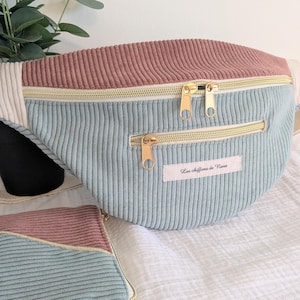 Peut inclure: Sac banane en velours côtelé aux couleurs pastel. Le haut est rose poudré, le corps principal bleu clair et les fermetures éclair dorées. Un petit étui assorti est également visible. Le texte "Les chiffons de Nana" est sur une petite étiquette.