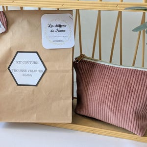 Op de afbeelding: Een bruine papieren zak met een zwart-wit label met de tekst "KIT COUTURE TROUSSE VELOURS ELISA" staat naast een roze corduroy etui met een gouden rits. Een kleine witte kaart met "Les chiffons de Nana" is ook zichtbaar.