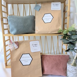May include: A display of corduroy pouches and craft kits on a bamboo shelf. The pouches are in muted teal and dusty rose, with a vertical ribbed texture. Kraft paper bags feature the text "KIT COUTURE TROUSSE VELOURS ELISA" and "Les chiffons de Nana".