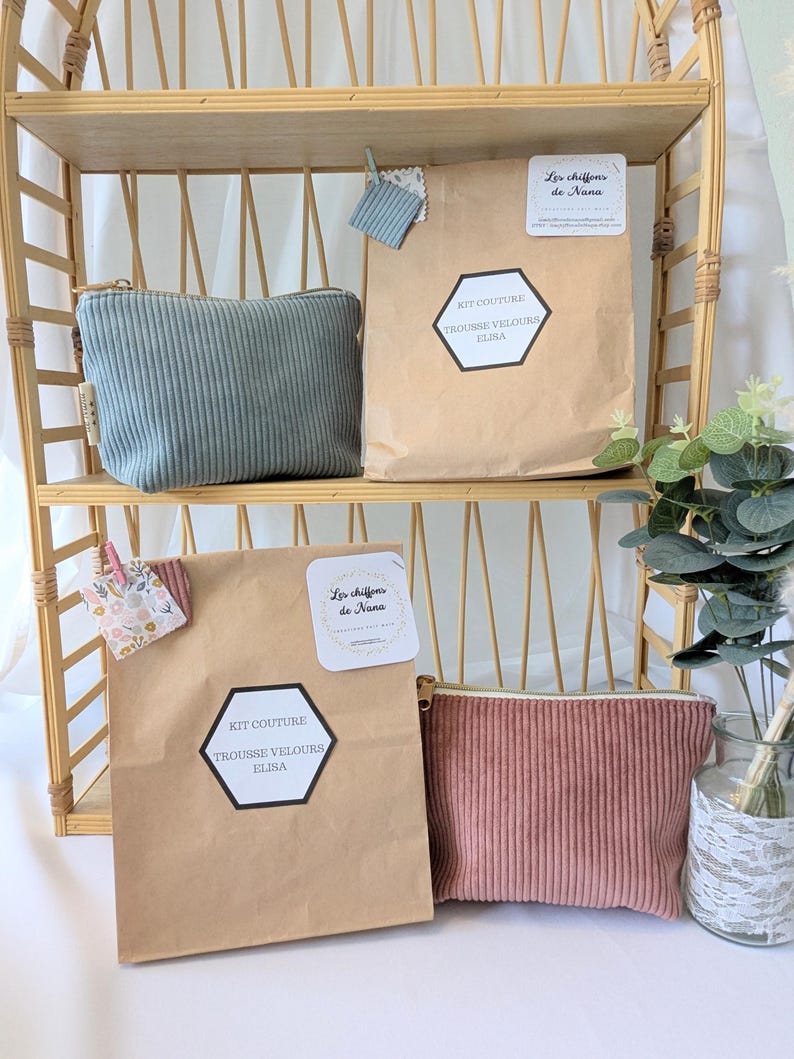 May include: A display of corduroy pouches and craft kits on a bamboo shelf. The pouches are in muted teal and dusty rose, with a vertical ribbed texture. Kraft paper bags feature the text "KIT COUTURE TROUSSE VELOURS ELISA" and "Les chiffons de Nana".