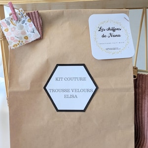 May include: A brown paper bag labeled "KIT COUTURE TROUSSE VELOURS ELISA" with a black and white hexagon-shaped label. A small fabric swatch with floral patterns and a pink corduroy swatch are clipped to the bag. A white tag with gold text reads "Les chiffons de Nana".