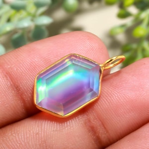 以下が含まれることがあります： 金色のペンダント。多面的な、虹色の宝石が特徴です。宝石は紫、青、緑など、さまざまな色を表示します。ペンダントは六角形で、チェーン用の小さなループが付いています。