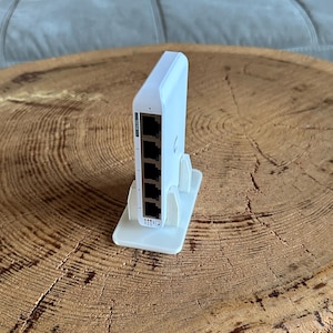 Può includere: Uno switch di rete bianco posizionato verticalmente su un supporto in plastica bianca abbinato. Il dispositivo presenta cinque porte Ethernet disposte in colonna, ciascuna numerata, con piccole spie luminose situate alla base delle porte.