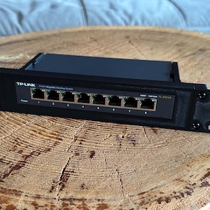 Può includere: Uno switch desktop Gigabit a 8 porte TP-Link nero montato in una staffa di montaggio a rack in metallo nero. Il pannello frontale presenta otto porte Ethernet numerate da uno a otto, una spia di alimentazione e il testo TP-Link 8-port Gigabit Desktop Switch.