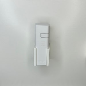 May include: White wall-mounted holder with a white smart home device. The device has buttons labeled "pairing", "cloud", "roster", and "power". The holder has the word "tado" printed on it.
