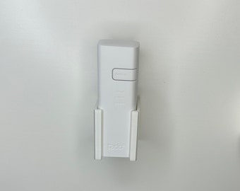 May include: White wall-mounted holder with a white smart home device. The device has buttons labeled "pairing", "cloud", "roster", and "power". The holder has the word "tado" printed on it.