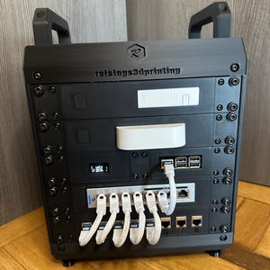 Pode incluir: Um dispositivo eletrônico preto de vários níveis com várias portas e cabos brancos. O dispositivo tem o texto "reisings3dprinting" e um logotipo na parte superior. Possui alças e é montado em uma superfície de madeira.