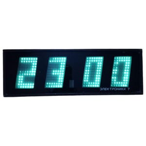 May include: A black digital clock displaying the time 23:00 in bright green LED lights. The clock face has four rectangular sections, each displaying a number. The text "ЭЛЕКТРОНИКА 7" is printed in white at the bottom.