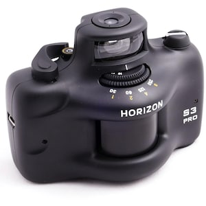 Könnte beinhalten: Schwarze Horizon S3 Pro Panorama-Kamera. Die Kamera hat ein geschwungenes Gehäuse mit einem prominenten Objektiv und einem Rad mit Geschwindigkeitseinstellungen. Das Wort "HORIZON" ist weiß gedruckt, und "S3 PRO" ist vertikal gedruckt. Sie hat einen Sucher und einen Auslöser.