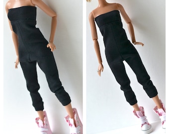 Könnte beinhalten: Ein schwarzer trägerloser Jumpsuit mit einem figurbetonten Oberteil und schmal zulaufenden Beinen. Der Jumpsuit wird von einer Puppe mit rosafarbenen Turnschuhen getragen.