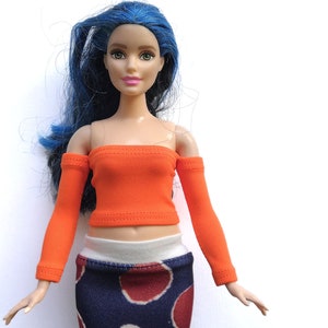 May include: A doll wearing an orange off-the-shoulder top with long sleeves and a blue and red polka dot skirt.