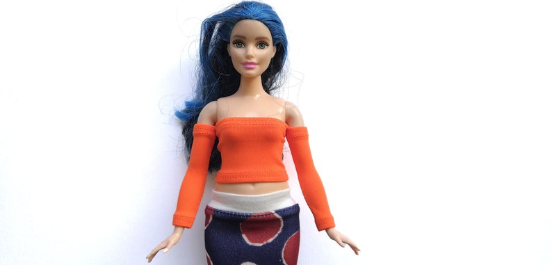 May include: A doll wearing an orange off-the-shoulder top with long sleeves and a blue and red polka dot skirt.