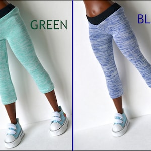 K&ouml;nnte beinhalten: Zwei Leggings f&uuml;r Puppen, eine gr&uuml;n und eine blau, mit einem schwarzen Bund. Die Leggings haben ein marmoriertes Muster. Die Puppe tr&auml;gt blaue Turnschuhe.