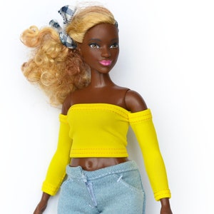 May include: A doll with brown skin and blonde curly hair wearing a yellow off-the-shoulder top with long sleeves and light blue jeans.