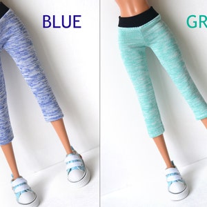 K&ouml;nnte beinhalten: Zwei Paar Leggings in Puppengr&ouml;&szlig;e, eine blaue und eine gr&uuml;ne, mit einem schwarzen Bund. Die Leggings haben ein marmoriertes Muster.