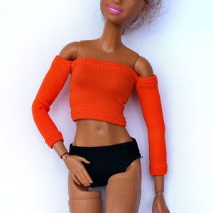 May include: A doll wearing an orange off-the-shoulder top with long sleeves and black bottoms.