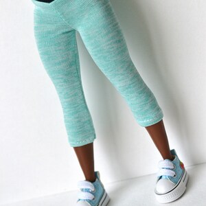K&ouml;nnte beinhalten: Eine tealblaue Leggings mit schwarzem Bund. Die Leggings besteht aus einem weichen, dehnbaren Material und hat einen dezenten Melange-Effekt. Die Leggings wird von einer Puppe mit brauner Haut getragen und wird mit hellblauen Turnschuhen kombiniert.