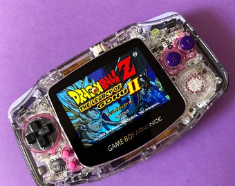 May include: A clear Game Boy Advance handheld gaming console with a pink and purple button set. The screen displays the game "Dragon Ball Z: The Legacy of Goku II" with the text "(c) 2003 Bird Studios/SHUEISHA, Toei Animation, GAME BOY ADVANCE".