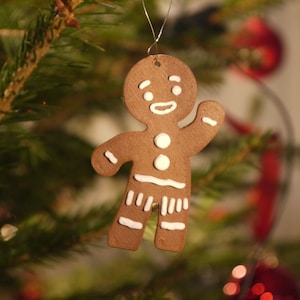 Könnte beinhalten: Ein Lebkuchenmann-Weihnachtsornament mit weißen Zuckergussdetails, das an einem Weihnachtsbaum hängt.