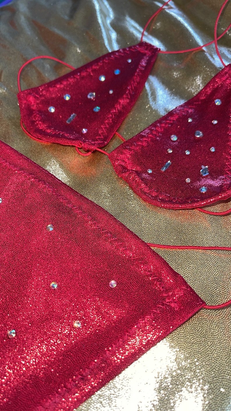 Peut inclure: Un ensemble de bikini rouge orn&eacute; de paillettes. Le haut pr&eacute;sente des bonnets triangulaires avec des liens, et le bas est assorti. Le tissu a une texture chatoyante, et le fond est une surface dor&eacute;e textur&eacute;e.