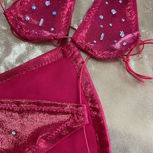 Peut inclure: Ensemble de bikini rose vif avec des embellissements scintillants. Le haut triangle et le bas sont orn&eacute;s de strass iris&eacute;s. Les bords sont bord&eacute;s d'une couture rose plus fonc&eacute;e. Le bikini est fait d'un tissu brillant et textur&eacute;.