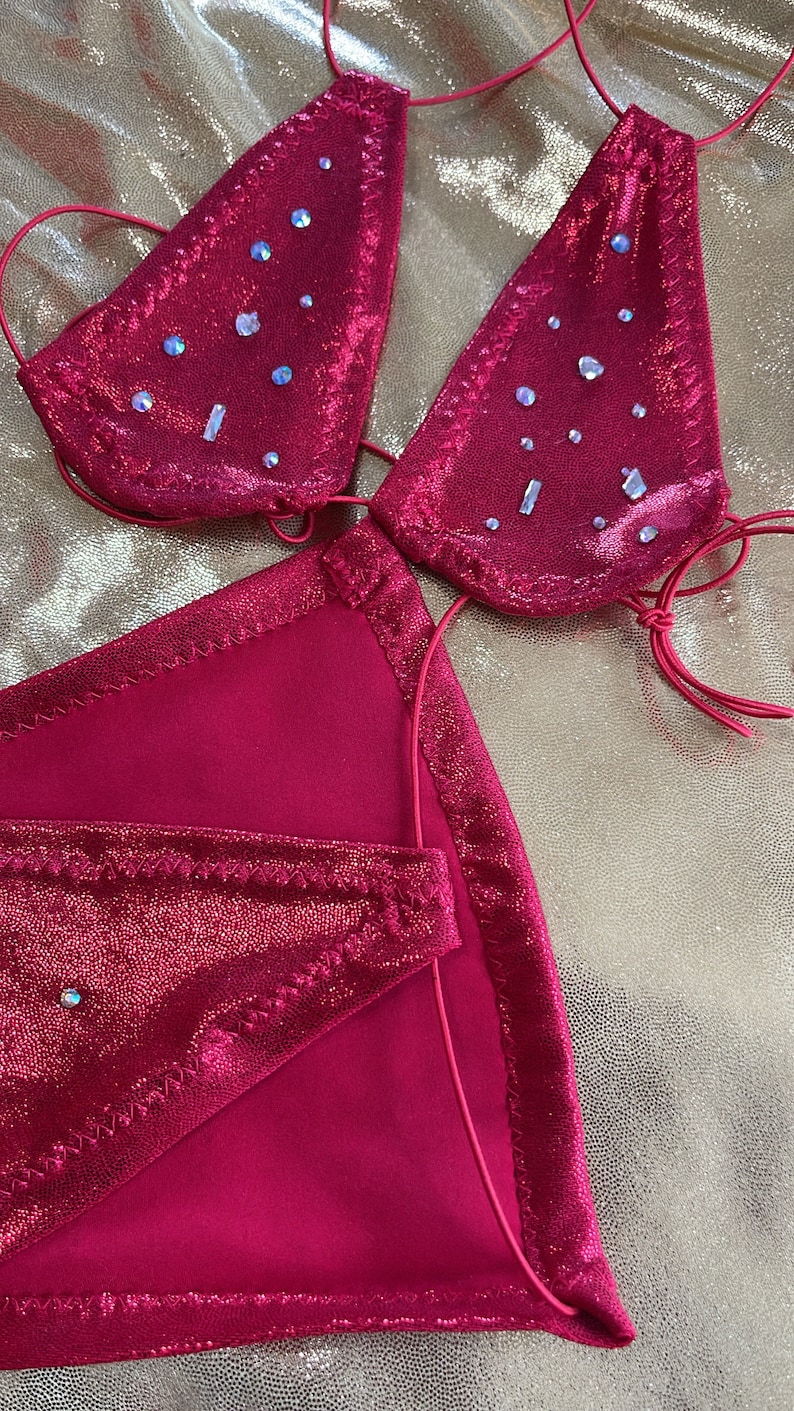 Peut inclure: Ensemble de bikini rose vif avec des embellissements scintillants. Le haut triangle et le bas sont orn&eacute;s de strass iris&eacute;s. Les bords sont bord&eacute;s d'une couture rose plus fonc&eacute;e. Le bikini est fait d'un tissu brillant et textur&eacute;.