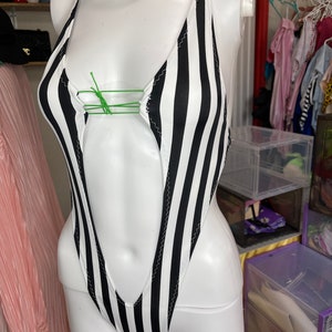 May include: A black and white striped swimsuit with a plunging neckline and a halter strap. The swimsuit is on a white mannequin.