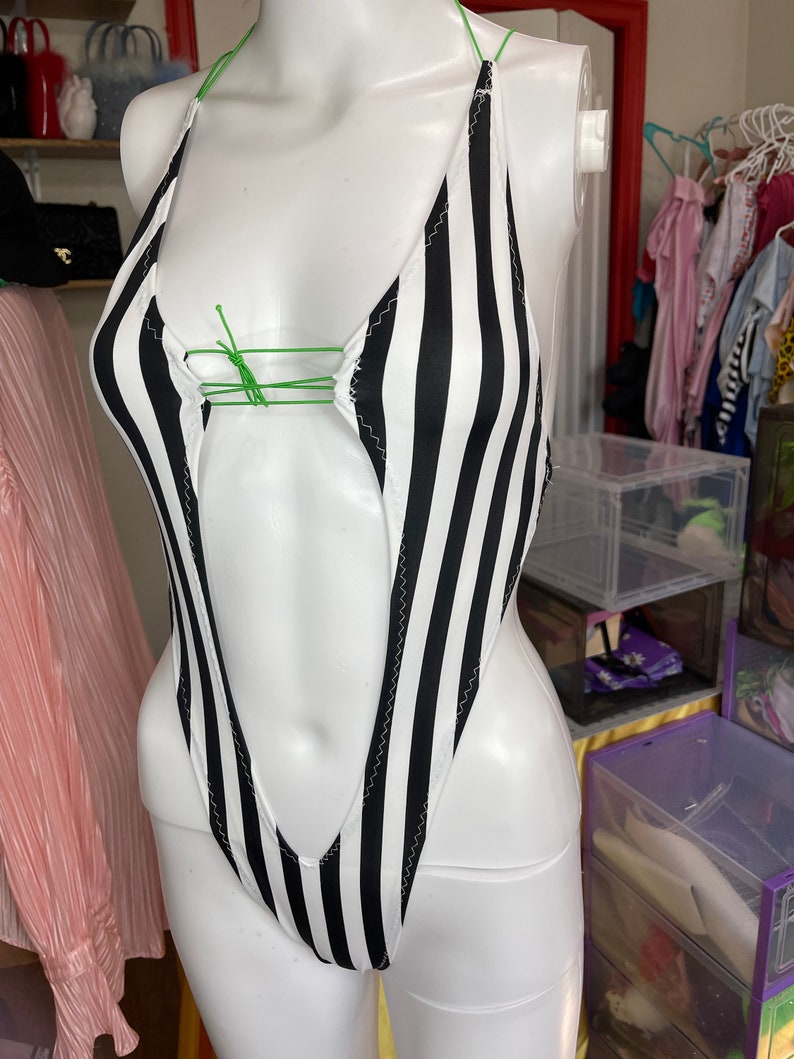 May include: A black and white striped swimsuit with a plunging neckline and a halter strap. The swimsuit is on a white mannequin.