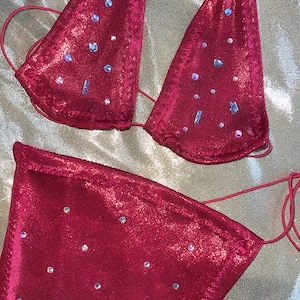 Peut inclure: Ensemble de bikini deux pi&egrave;ces magenta. Le haut triangle et le bas taille haute sont orn&eacute;s de strass iris&eacute;s. Le bikini est fait d'un tissu brillant et textur&eacute; et comporte de fines bretelles r&eacute;glables. Un article de maillot de bain d'&eacute;t&eacute;.
