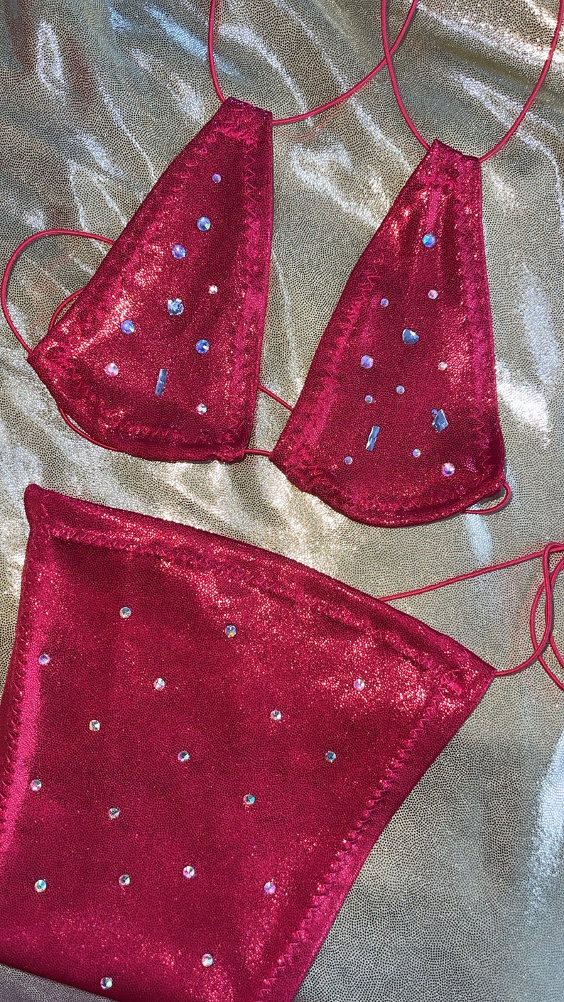 Peut inclure: Ensemble de bikini deux pi&egrave;ces magenta. Le haut triangle et le bas taille haute sont orn&eacute;s de strass iris&eacute;s. Le bikini est fait d'un tissu brillant et textur&eacute; et comporte de fines bretelles r&eacute;glables. Un article de maillot de bain d'&eacute;t&eacute;.