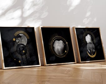 Puede incluir: Tres impresiones artísticas enmarcadas con diseños celestiales abstractos. Cada impresión presenta un fondo negro con formas circulares y de media luna doradas y blancas. Los marcos son de color madera clara y las impresiones están apoyadas contra una pared blanca.