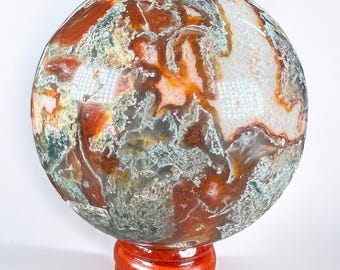 May include: A large, round, green, orange, and white agate sphere on a wooden stand. The sphere has a unique, swirling pattern.