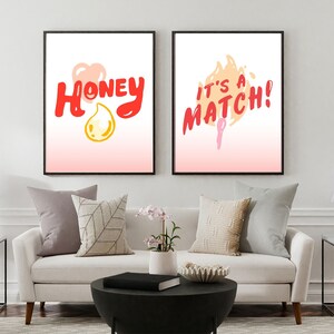 May include: Two framed prints with a pink and white gradient background. The left print features the word "Honey" in red with a yellow heart and a yellow teardrop. The right print features the text "It's a Match!" in red with a flame graphic.