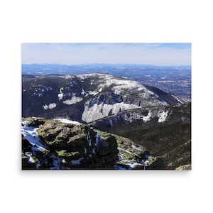May include: A snowy mountain peak with a view of a valley and distant mountains in the background. The mountain is covered in snow and ice, and the sky is blue.