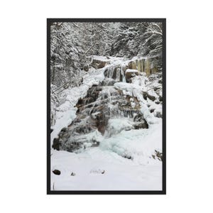 May include: A framed photograph of a waterfall cascading down a rocky slope, partially frozen with ice and snow. The surrounding trees are covered in snow, creating a winter landscape scene.