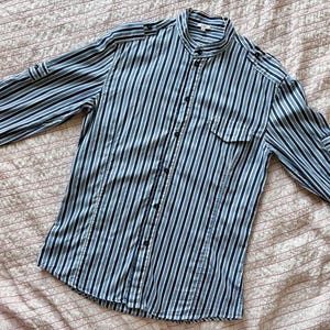 May include: A blue and white striped long-sleeved shirt with a mandarin collar and button closure. The shirt has a pocket on the left side.
