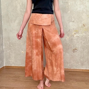 May include: A black short-sleeved t-shirt paired with wide-leg trousers in a mottled terracotta orange color. The trousers feature a high-waisted wrap-style panel with stitched geometric detailing across the front and a central vertical slit.