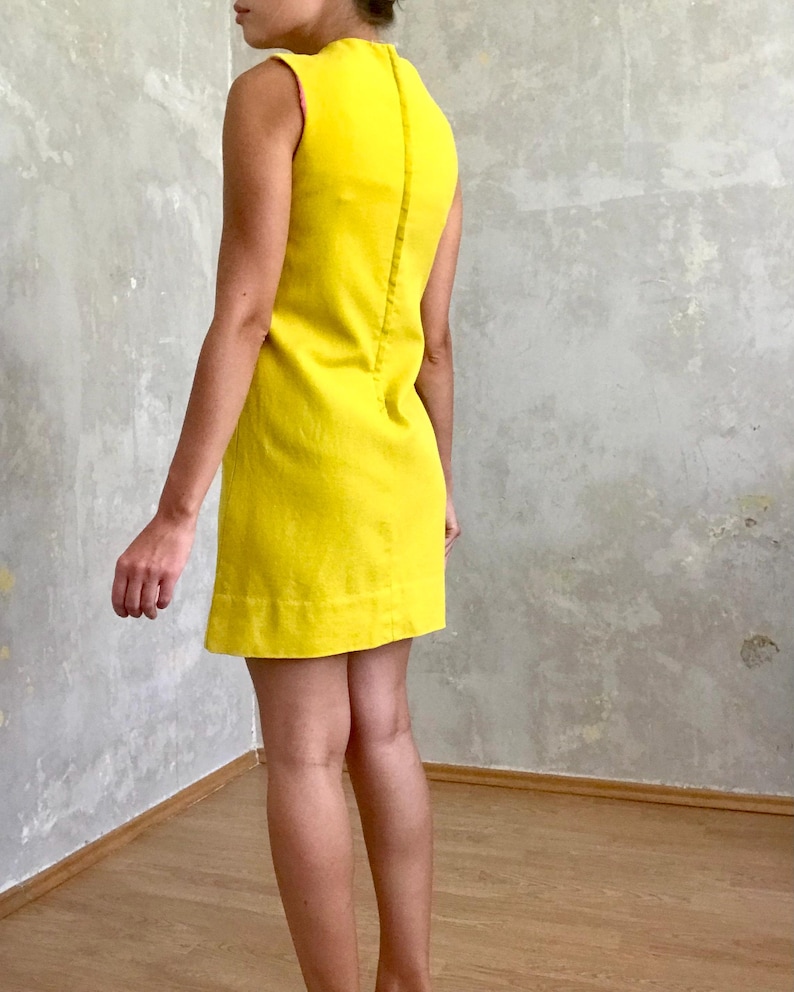 May include: A sleeveless yellow mini dress with a simple design. The dress is made of a smooth, lightweight fabric.