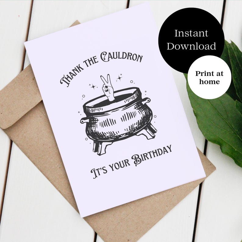 May include: A white card with a black and white illustration of a hand making a peace sign sticking out of a cauldron. The text on the card reads "Thank the Cauldron It's Your Birthday".