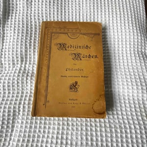 May include: A vintage book titled "Medizinische Märchen" by Philander. The book is bound in yellow paper with a decorative border and a small illustration of a bird on the cover. The book was published in Stuttgart in 1895.